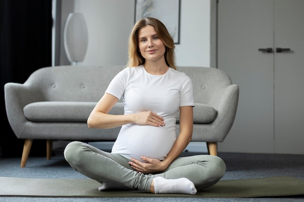 Smiling pregnant woman touching her belly, meditation sitting in lotus pose. Pregnancy, motherhood