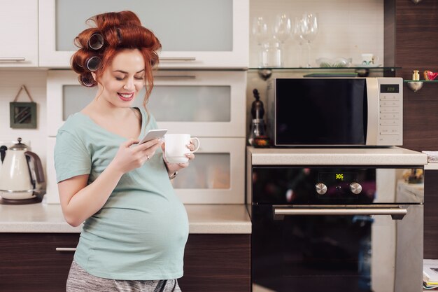 Donna incinta sorridente che per mezzo di uno smartphone