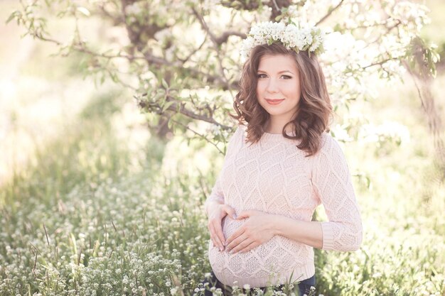 Smiling pregnant woman wearing knitted sweater making heart with hands outdoors