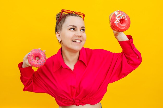 Фото Улыбающаяся беременная женщина с сладкими пирогами в руках на желтом фоне вкусные сладкие пончики в руках женщины вредная еда