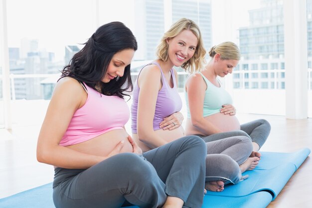 Photo smiling pregnant women sitting in yoga class touching their bumps