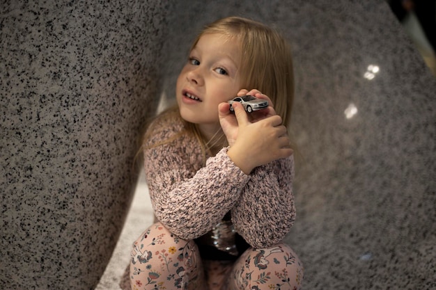 Smiling preschool girl holding a model car against a marble wall