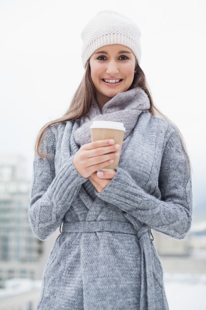 コーヒーを持って冬の服を着たかわいらしいブルネット