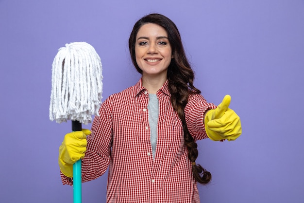 Sorridente donna delle pulizie piuttosto caucasica con guanti di gomma che tiene mop e fa il pollice in alto