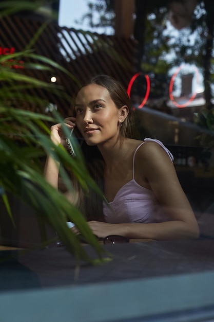 Smiling pretty lady calling by phone shot through window glass outside of cafe