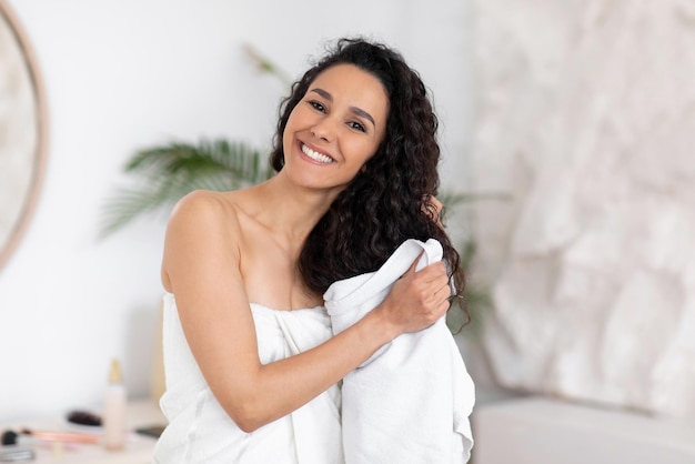 Smiling pretty millennial european brunette woman in towel dries curly long hair after shower in