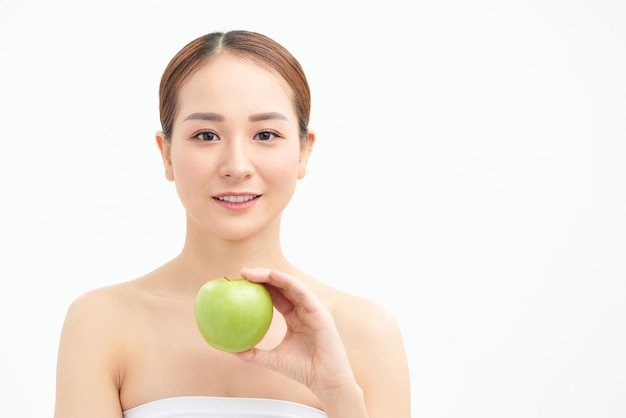 Sorridente modello grazioso che tiene mela mentre posa su sfondo bianco