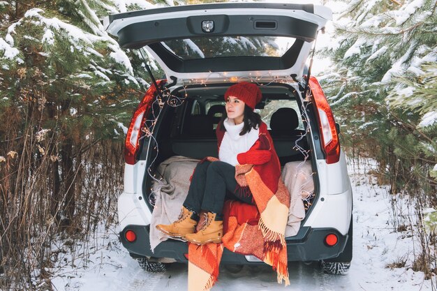 Smiling pretty woman in car trunk at snowed winter forest copy space