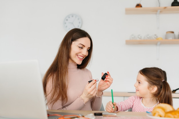 Fare grazioso sorridente della donna compone mentre si siede con la sua piccola figlia alla cucina durante la prima colazione.