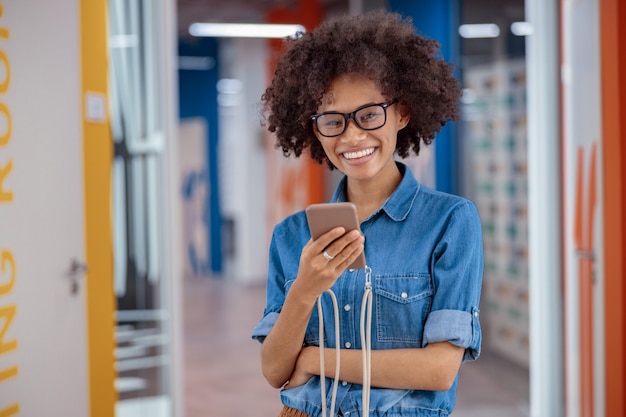 Smiling pretty woman holding mobile phone in office hall