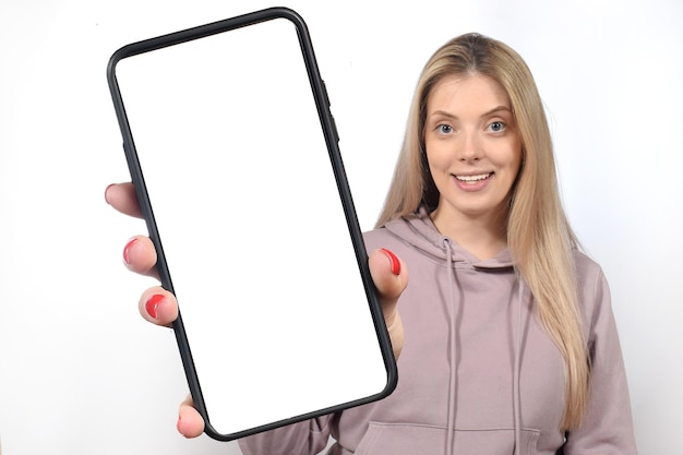 Фото Улыбающаяся красивая женщина держит смартфон с белым пустым экраном устройства в руке рядом с камерой