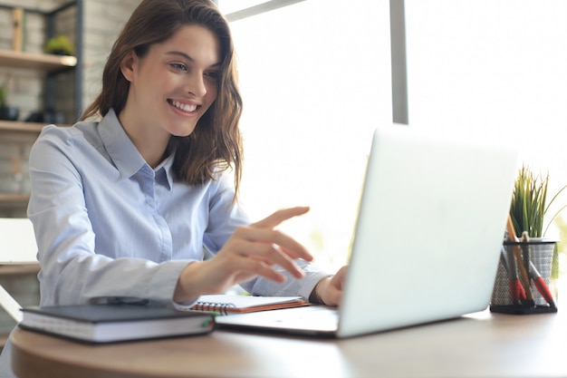 Sorridente bella donna seduta al tavolo, guardando lo schermo del laptop. felice imprenditore che legge un messaggio di posta elettronica con buone notizie, chatta con i clienti online.