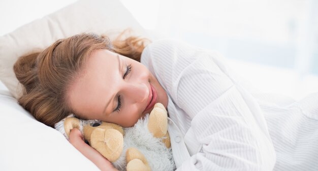 Smiling pretty woman sleeping embracing a plush sheep