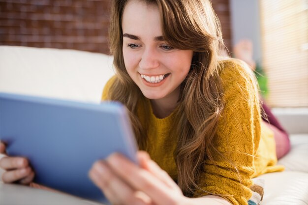 Donna graziosa sorridente che utilizza compressa sullo strato nel salone