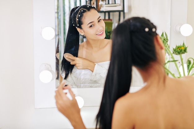 Smiling pretty young Asian woman brushing hair