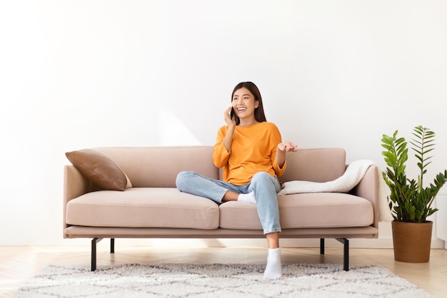 Photo smiling pretty young asian woman talking on phone at home