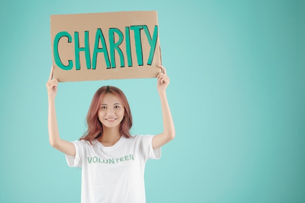 Smiling pretty young female volunteer holding charity paper sign above her head