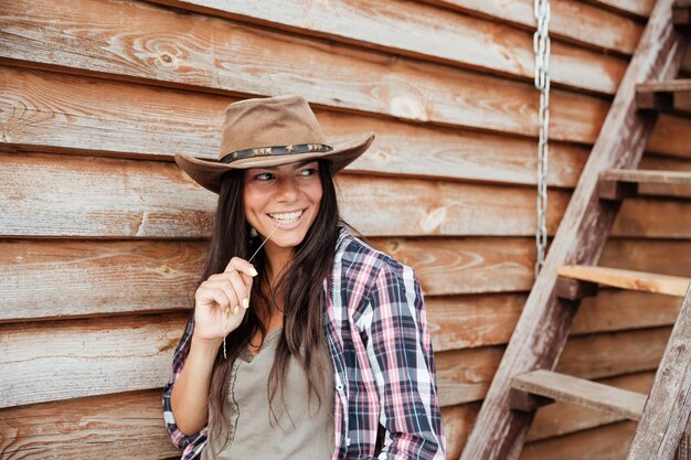 Smiling pretty young woman cowgirl in hat standing near the house