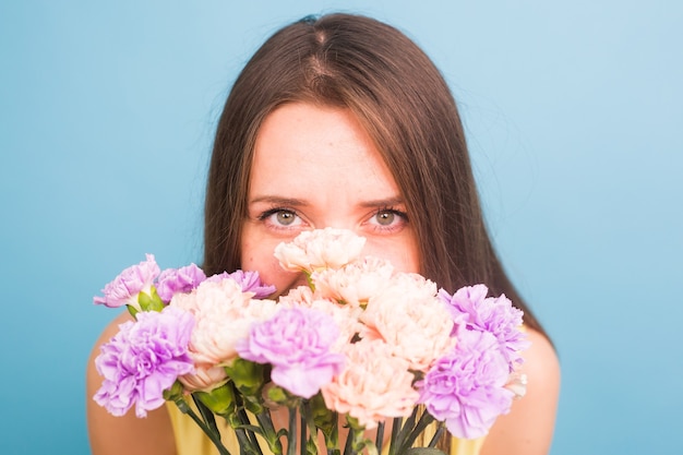 青い背景の上に花の花束を保持しているかなり若い女性の笑顔。