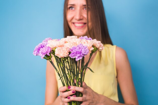 青い背景の上に花の花束を保持しているかなり若い女性の笑顔。