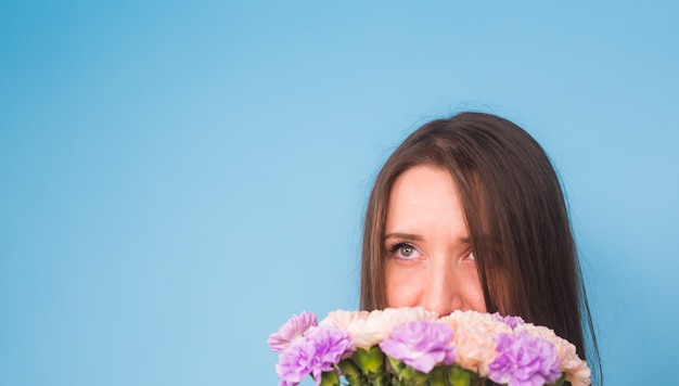 青い背景の上に花の花束を保持しているかなり若い女性の笑顔。