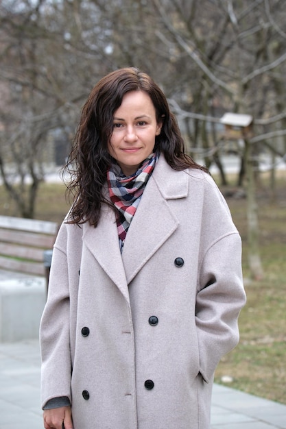 Sorridente bella giovane donna con lunghi capelli scuri in abiti alla moda in piedi all'aperto in una giornata di sole primaverile