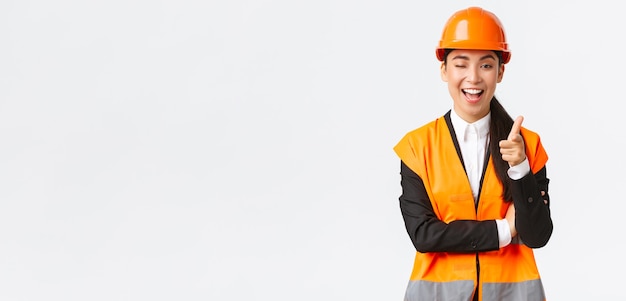 Smiling professional asian female construction manager in safety helmet and reflective jacket inviti...