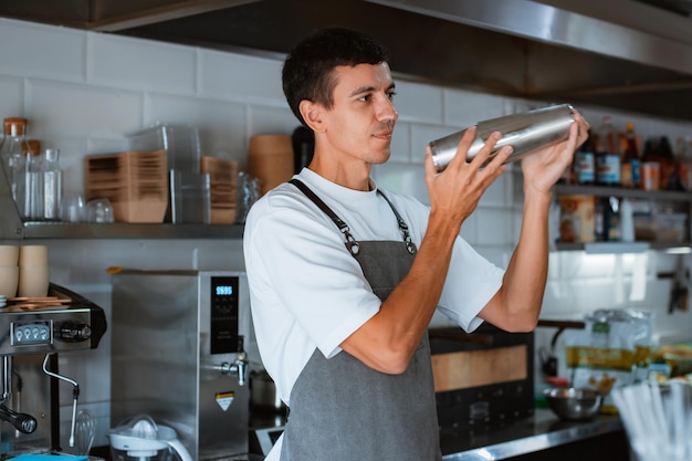 Улыбающийся профессиональный бариста-мужчина готовит фраппе с карамельным льдом во время работы в местной кофейне