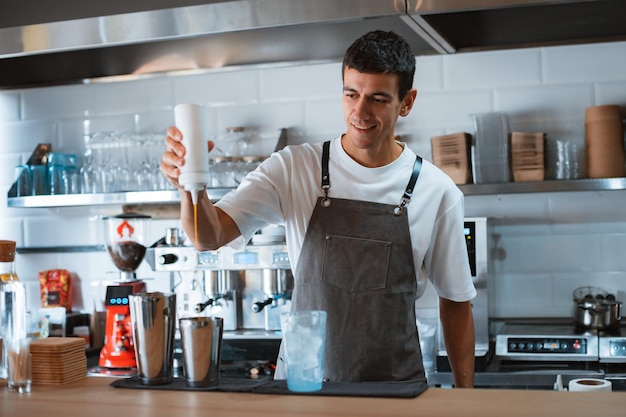 Smiling professional male barista making caramel iced frappe while working in local coffee shop