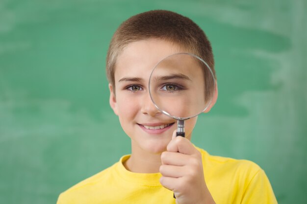 Smiling pupil looking through magnifier in a classroom 