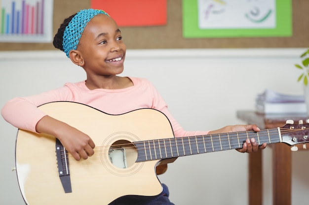 Smiling pupil playing guitar in a classroom