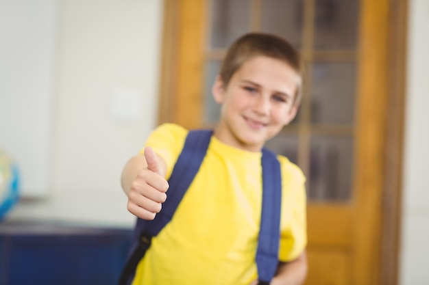 Allievo sorridente con la cartella che fa i pollici su in un'aula