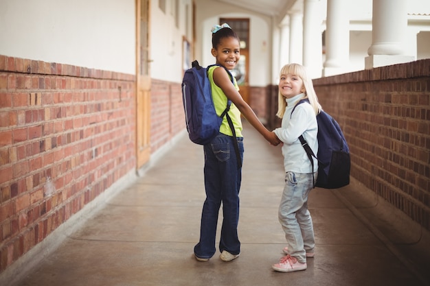 Smiling pupils holding hands at corridor