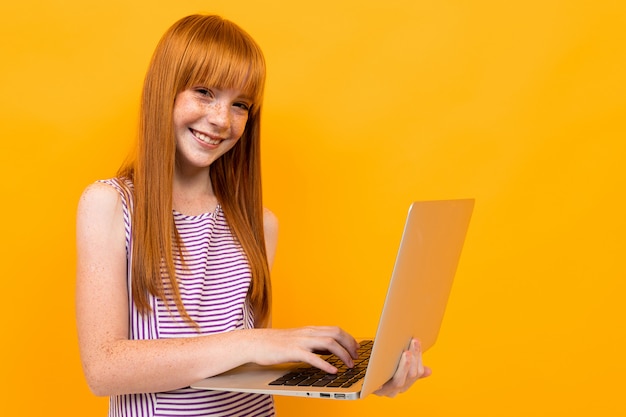 Smiling red-haired girl chatting on a laptop on a yellow banner background