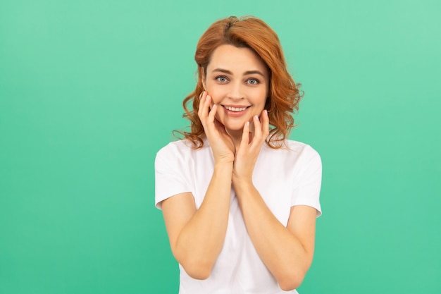 Smiling redhead girl with curly hair touch her perfect skin on blue background copy space skin and hair