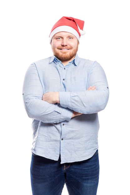 Smiling redhead man with a beard in a blue shirt and in a Santa Claus hat. Close-up. Isolated over white wall. Vertical.