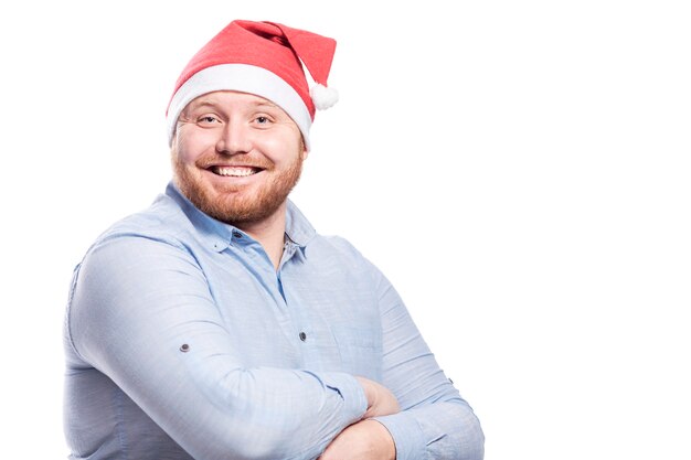 Smiling redhead man with beard in santa claus hat. Close-up. Space for text. Isolated over white wall.