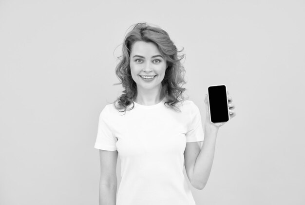 Smiling redhead woman chatting in smartphone or make online shopping on yellow background communication