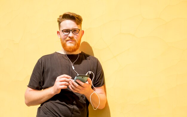 Il giovane sorridente della testarossa con una barba usa un telefono cellulare.