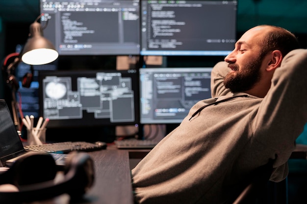 Smiling relaxed coder sitting laid back on chair, feeling pleased about software development work in office. Enjoying server programming success late at night, server code html script.