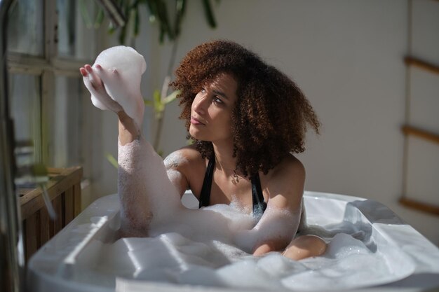 Photo smiling and relaxing african american woman bathing in a tub full of foam amazing time lifestyle people concept