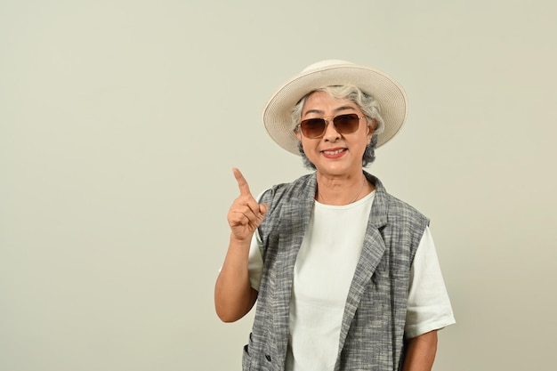 Smiling retired woman in sunglasses and hat pointing aside shows space for your advertisement or promotional text