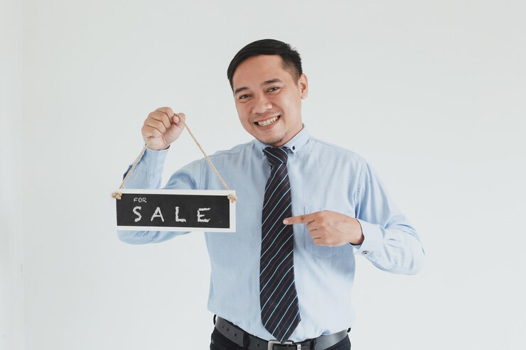 Photo 戴著藍色衫和帶的笑容銷售員,在白色背景上舉著 sale 招牌牌姿態