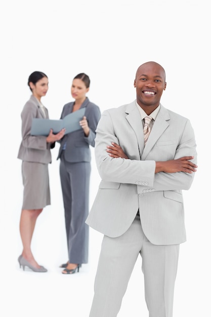 Smiling salesman with arms crossed and co-workers behind him