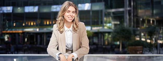 Photo smiling saleswoman in beige suit leans on handrail has a rest on city street