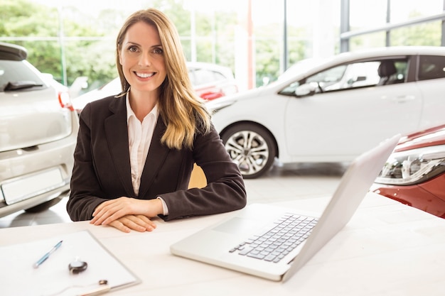 Smiling saleswoman behind her desk at new car showroom