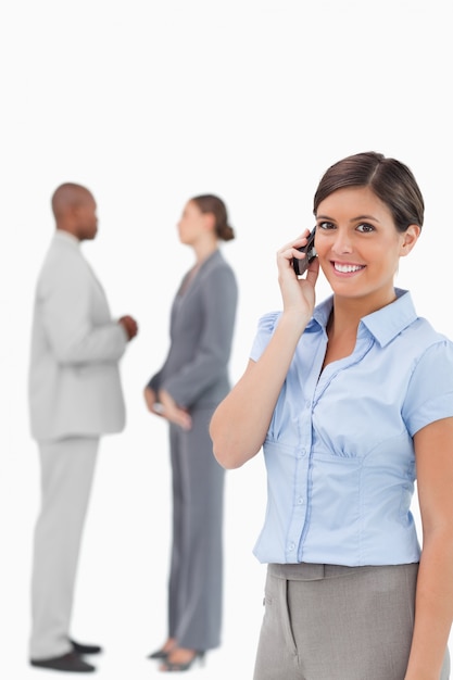 Smiling saleswoman on the phone with associates behind her