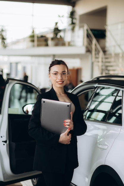 Smiling saleswoman typing on her laptop at new car showroom