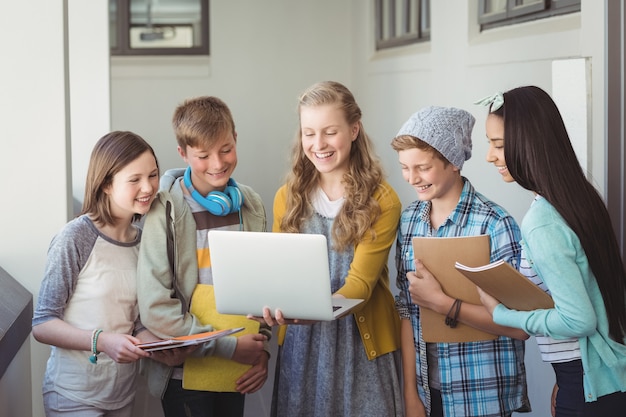 Studenti di scuola sorridente che utilizzano computer portatile in corridoio