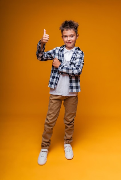 A smiling schoolboy in a plaid shirt and a white Tshirt stands with his arms crossed on his chest isolated on a yellow background portrait of a boy